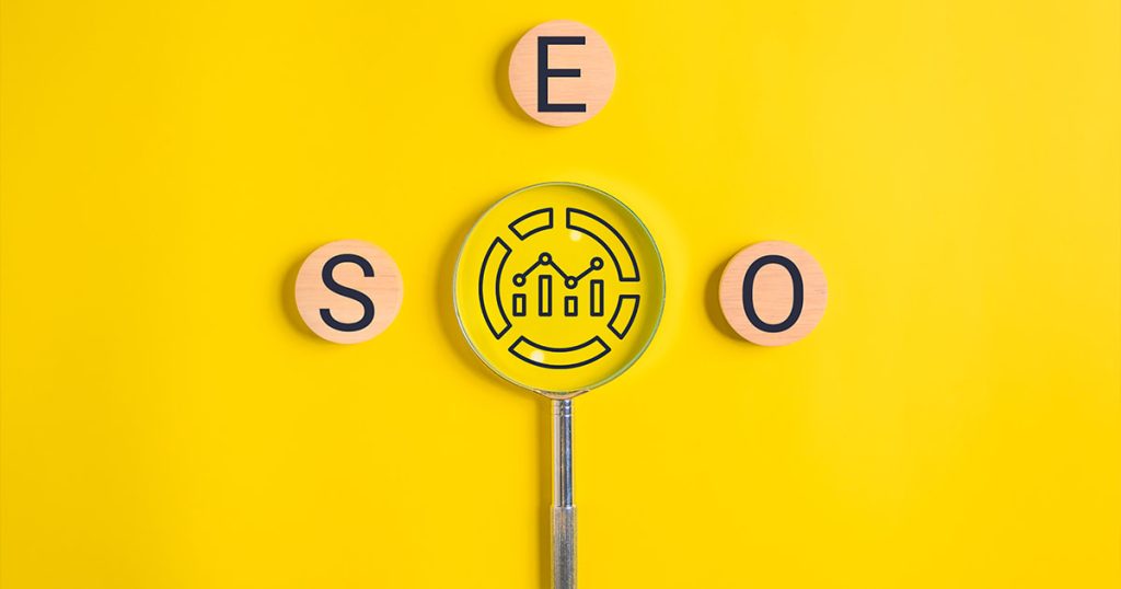 Lente di ingrandimento su sfondo giallo circondata da tessere in legno che formano la parola SEO